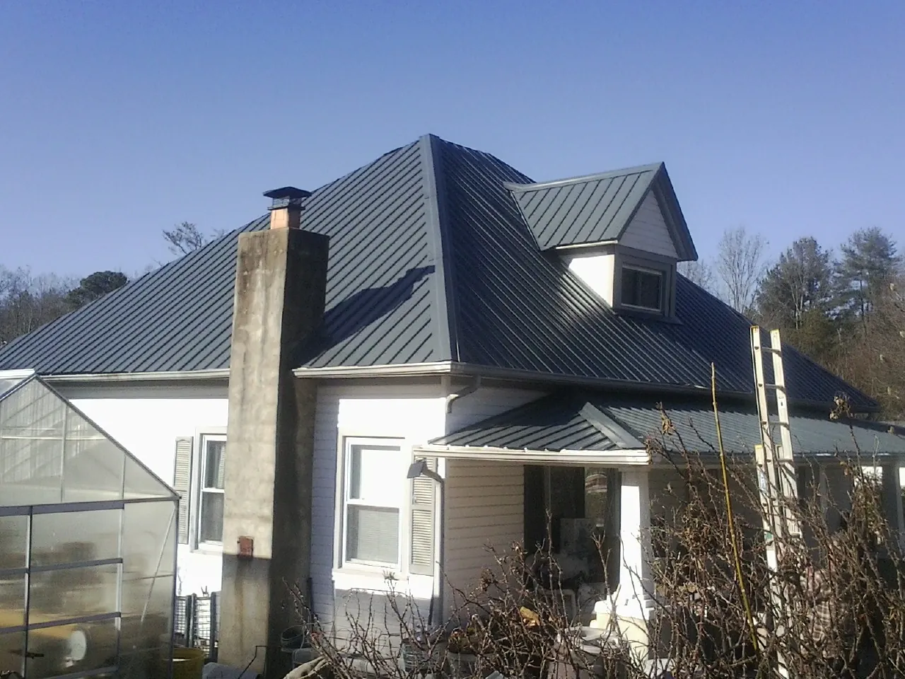 Dark blue standing seam metal roof on a white farmhouse with dormer — Slate & Tile Roof Repair by Roofing Brothers in Paul Smiths