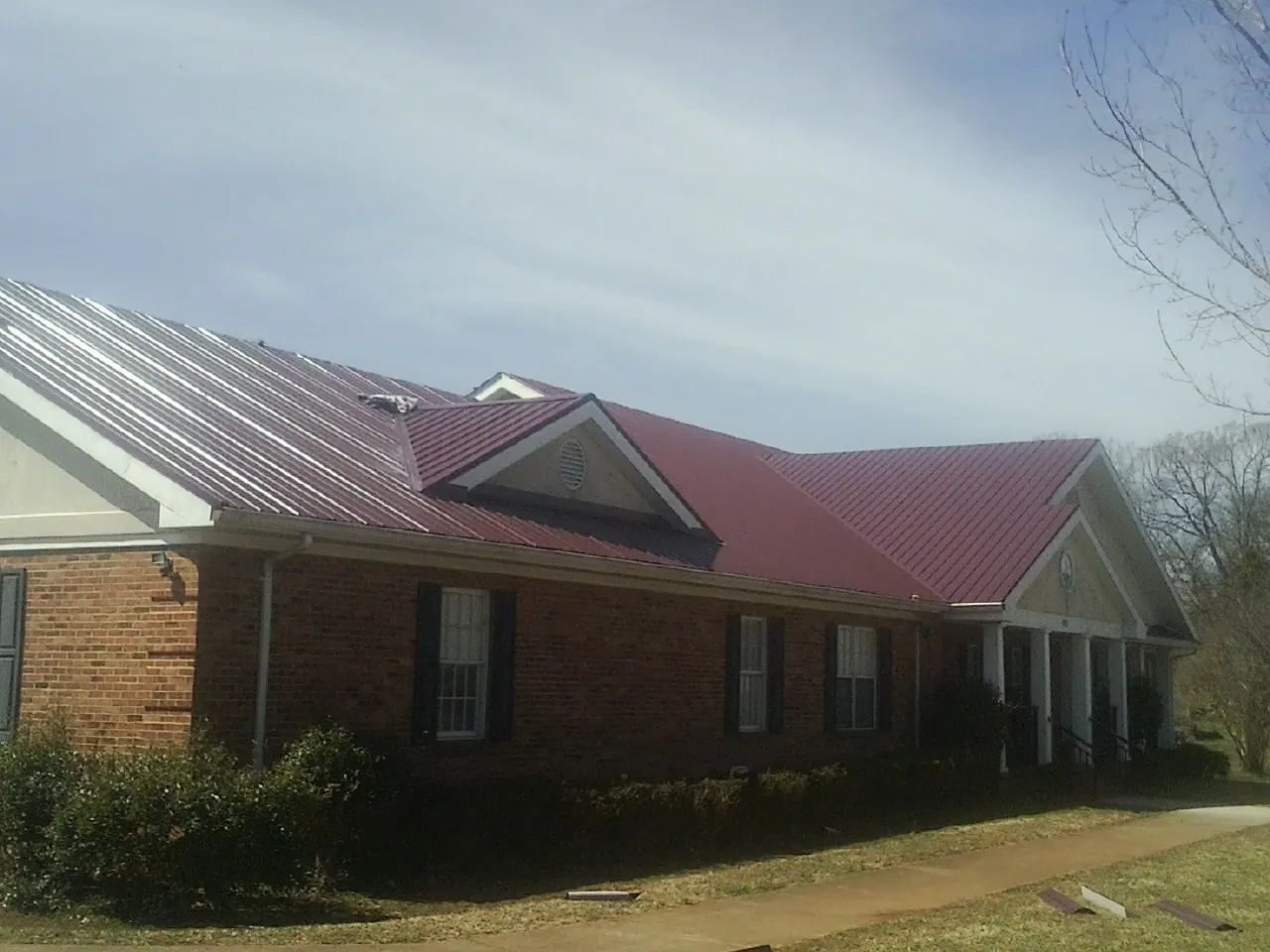 Red metal roof with gabled entries on a long brick building, from a Hail Damage Roof Repair job in Paul Smiths