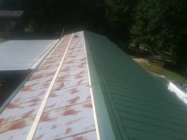 Old rusted panels beside newly installed green metal roofing — Wind Damage Roof Repair by Roofing Brothers in Paul Smiths