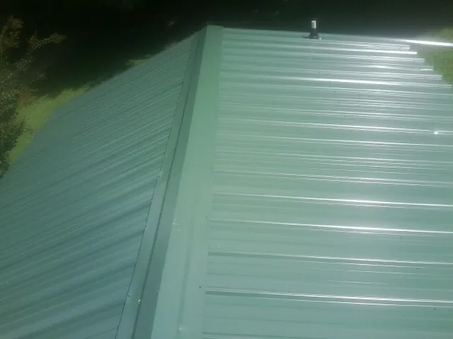 New green metal panels meeting at the ridge of a roof — Flat Roof Repair work by our crew in Paul Smiths