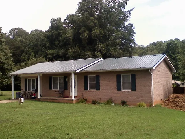 Gray metal roof on a brick ranch house with a side carport in Paul Smiths
