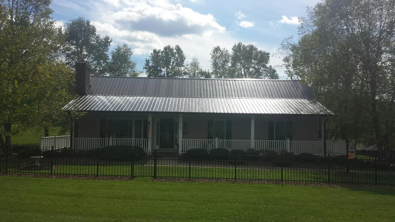 Gray metal roof on a brick ranch with a full width front porch — Gutter Guard Installation work by our crew in Paul Smiths