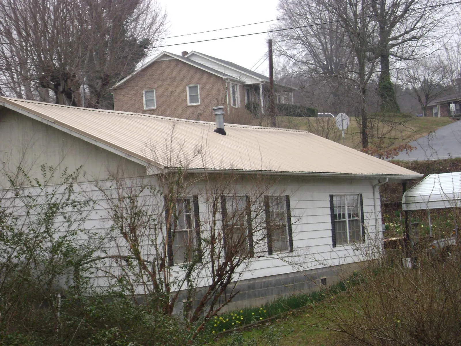 Tan metal roof on a white sided house set into a hillside — Commercial Roofing by Roofing Brothers in Paul Smiths
