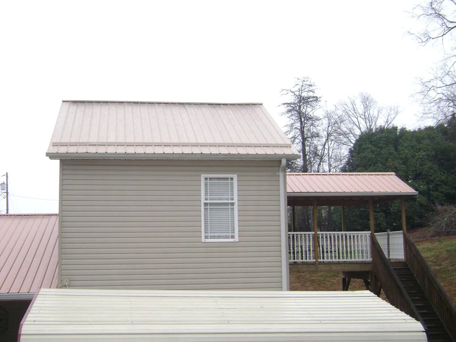 Tan metal roofs on a two story addition and attached porch, from a Roof Replacement job in Paul Smiths